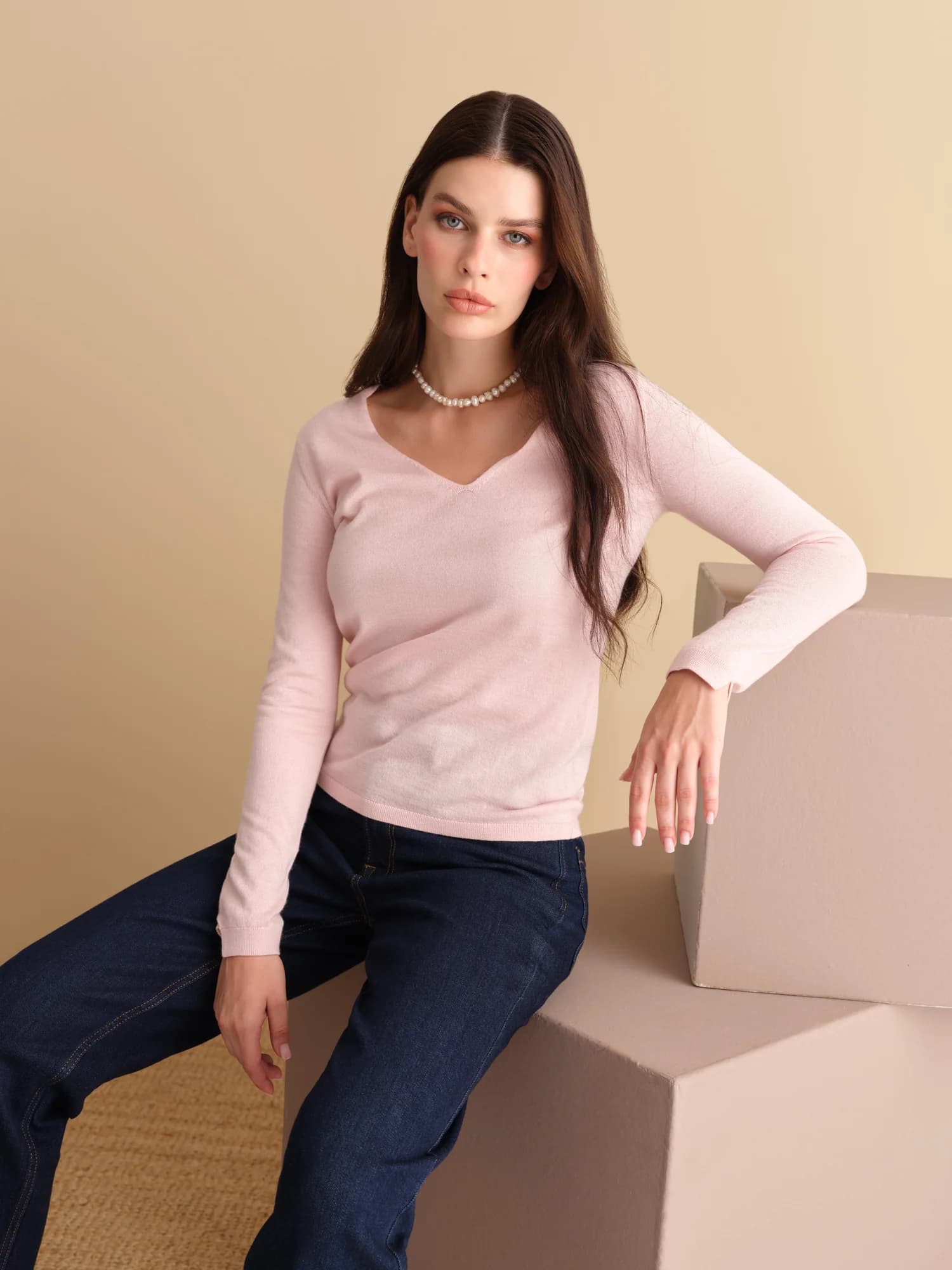 Pembe kazak ve kot pantolon giyen model, bej fonda oturuyor