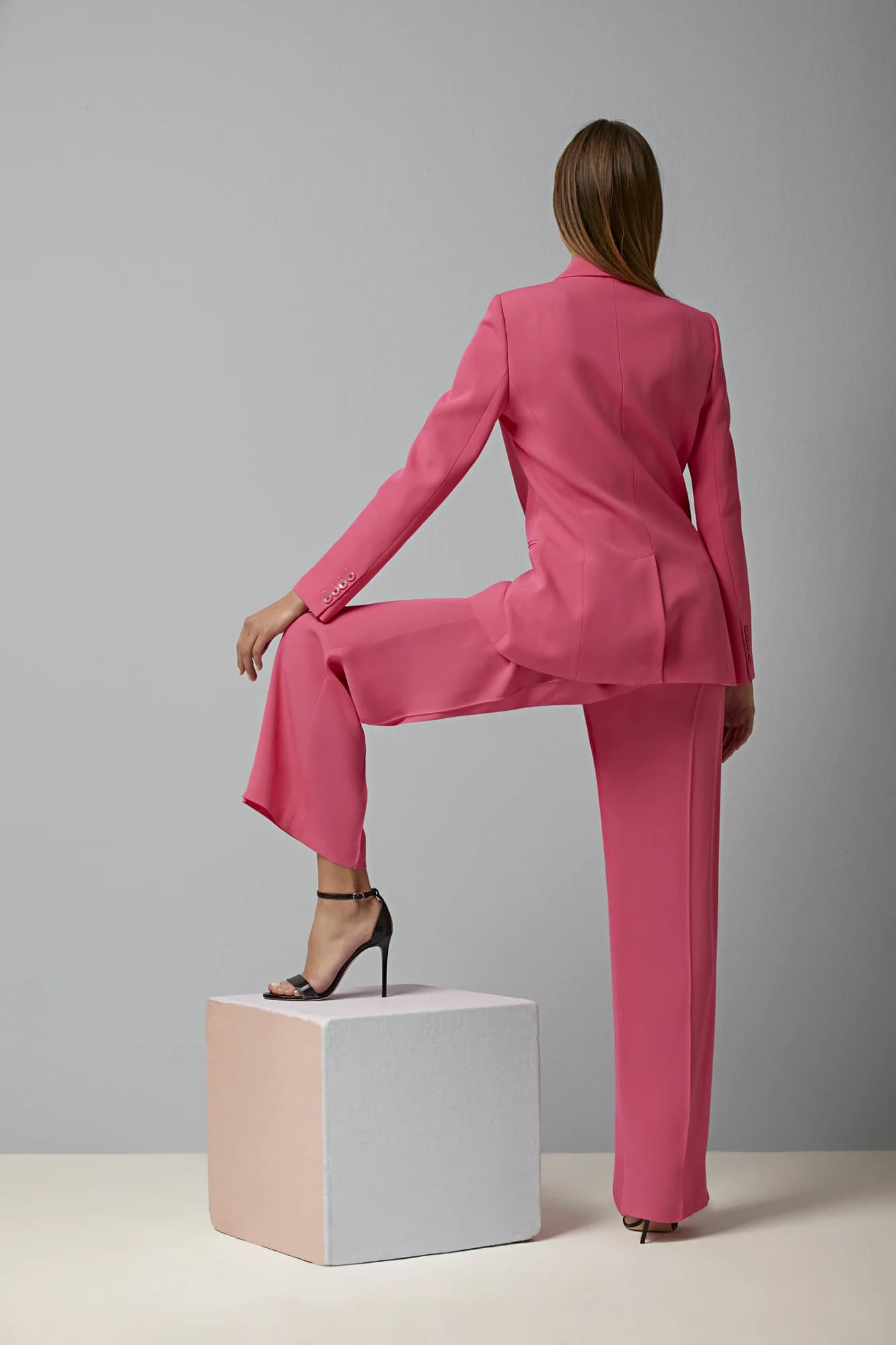 Pembe takım elbiseli model, gri fonda küçük kaide üzerinde